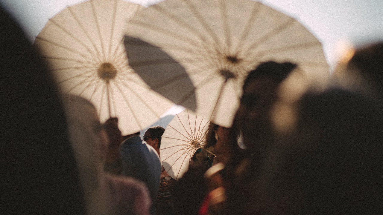 Convidados de casamento com sombrinhas em luz de fim de tarde